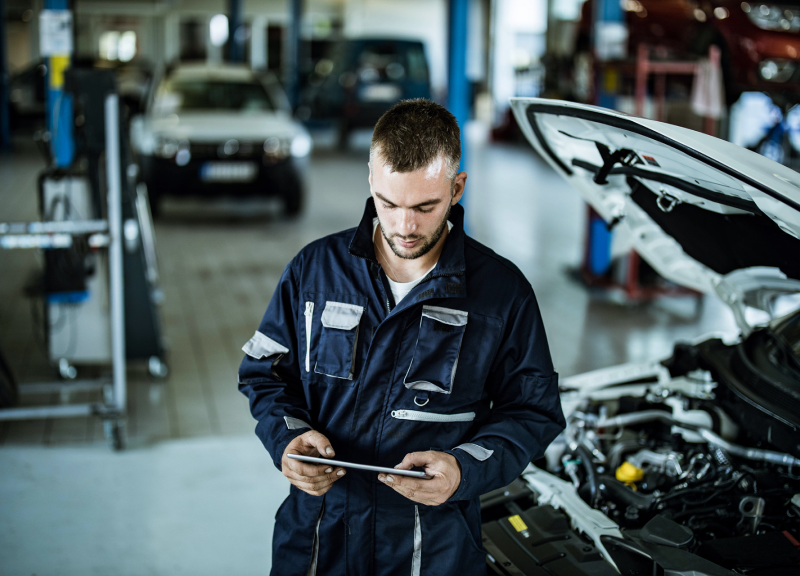 Mechanik przeprowadzający diagnostykę na tablecie stojącym obok otwartej maski samochodu